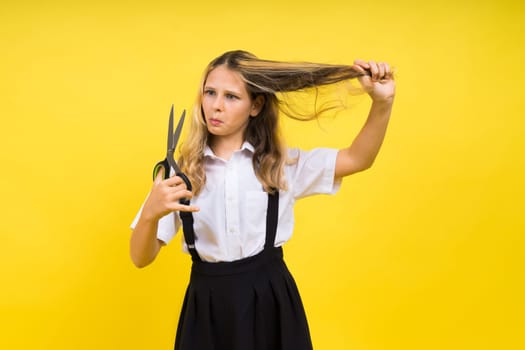A young girl about to cut her own hair with pair of scissors, isolated against yellow background