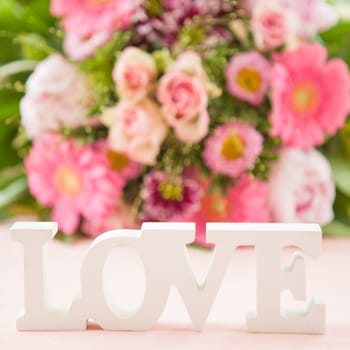 LOVE in front of colorful bouquet of flowers on pink