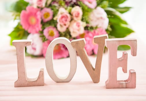 LOVE in front of colorful bouquet of flowers on pink