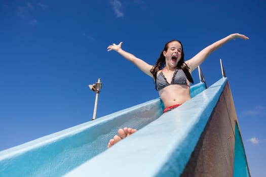 Girl teenager on swimming pool water slide summer fun.
