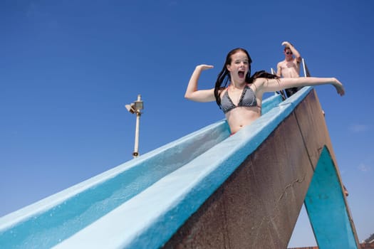 Girl teenager on swimming pool water slide summer fun.