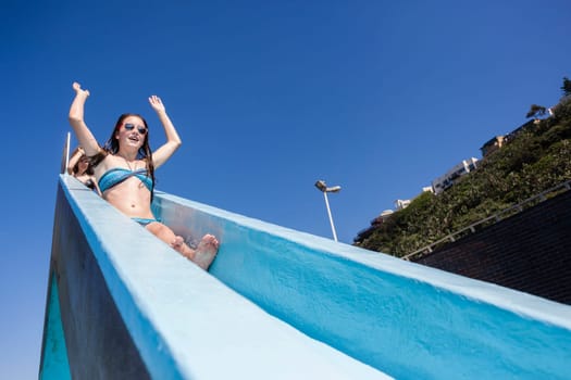 Girl teen on swimming pool water slide summer fun.