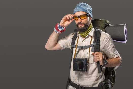 Portrait of a male fully equipped tourist with backpack and the camera on gray background