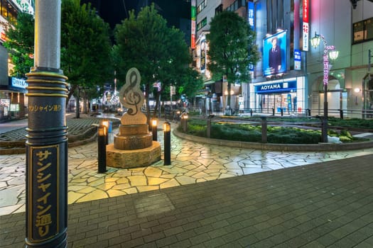 ikebukuro, japan - december 31 2012: Street lamp pole of Sunshine Street in front of a marble monument shaped in treble clef at the east exit of Ikebukuro station in Tokyo at night.