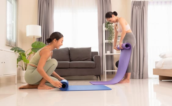 Two happiness young yoga women rolling mat after doing yoga exercise workout in living room at home. Healthy life and fitness training workout concept