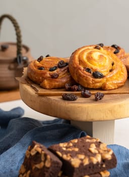 Baked sweet cinnamon buns with raisins on wooden board and chocolate brownies with cashew nut. Fresh bakery bread for breakfast