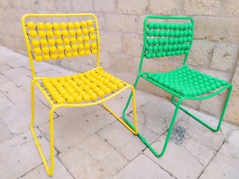 Two chairs are lined up on the marble pavement. Yellow and green empty massage chairs with pimples. Dubrovnik, Croatia. Creative non-standard interior