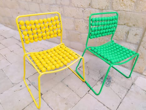 Two chairs are lined up on the marble pavement. Yellow and green empty massage chairs with pimples. Dubrovnik, Croatia. Creative non-standard interior