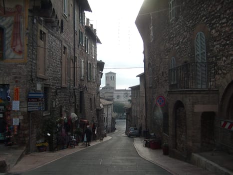 Assisi, Italy, December 10, 2020. Streets of Assisi, along which a group of tourists walk. Ancient buildings, close to each other. People on excursions. Narrow street.