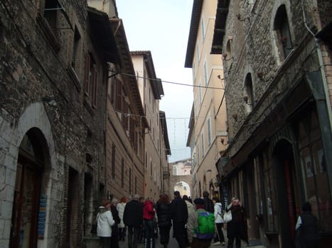 Assisi, Italy, December 10, 2020. Streets of Assisi, along which a group of tourists walk. Ancient buildings, close to each other. People on excursions. Narrow street.