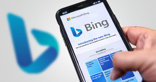 Redmond, US, Feb 2023: A hand holding a phone with the Microsoft Bing website on the screen. White background with blurred Bing logo. Bing is a search engine recently integrated with AI chatbot