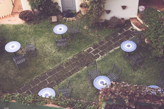 Vintage terrace patio with table and rattan chairs surrounded by lush greenery, high angle view. Relaxing area