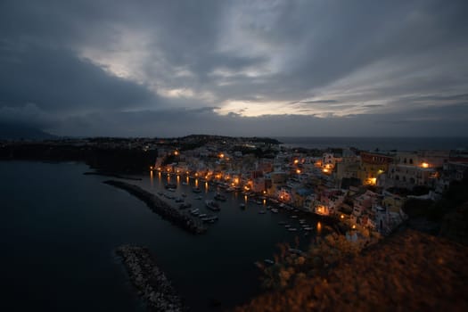 View of the Port of Corricella with lots of colorful houses after sunset in Procida Island, Italy.