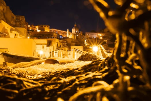 Fishing nets the Port of Corricella with lots of colorful houses after sunset in Procida Island, Italy.
