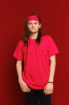 Three quarter portrait of positive guy wearing red band on head and t-shirt, standing against red wall