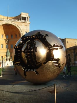 Vatican City, Rome, Italy - November 01, 2019 a golden metal ball representing the broken planet Earth. The insides of the planet are like a clockwork. Tourists take pictures.