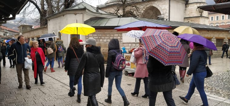 Sarajevo, Bosnia and Herzegovina, March 8, 2020. People on the central streets of Sarajevo. Tourists walk around Bascarsija. Gazi Husrev-begova dzamija mosque. People with umbrellas