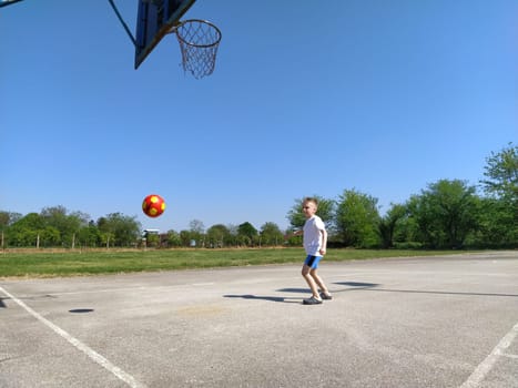 Sremska Mitrovica, Serbia. June 6, 2020. Sports games on the sports ground in the summer. The child plays with a ball. Schoolboy boy playing basketball during summer holidays