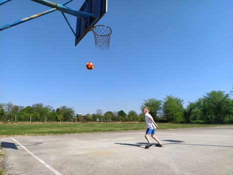 Sremska Mitrovica, Serbia. June 6, 2020. Sports games on the sports ground in the summer. The child plays with a ball. Schoolboy boy playing basketball during summer holidays