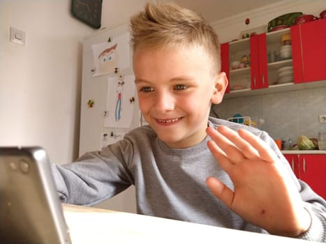 Sremska Mitrovica, Serbia, May 20, 2020 Blond boy with laptop. The child looks at the monitor and waves his hand as a greeting.