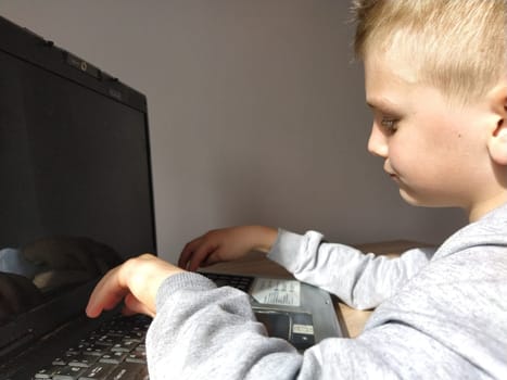 Sremska Mitrovica, Serbia, May 20, 2020 Blond boy with laptop. The child looks at the monitor and types on the keys.