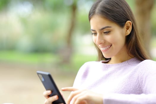 Happy woman checking cell phone in a park