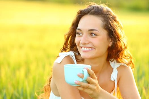 Happy woman holding coffee cup in a beautiful field at sunset