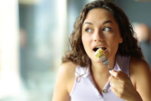 Front view portrait of a woman eating omelette looking at side in a restaurant