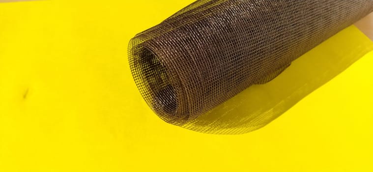 Roll of window screen, closeup. Roll of brown mosquito nets. Barrage mesh. Grid on yellow background.