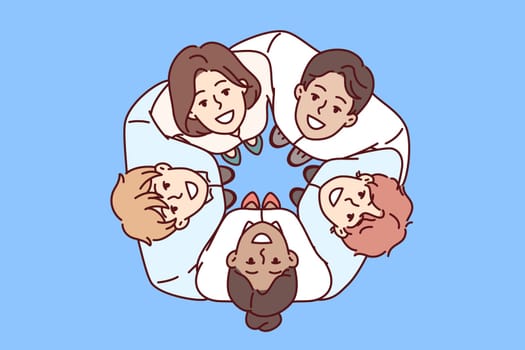 Team of young diverse businesspeople stand in circle and hugging colleagues look up during team building. Happy businesspeople take pride in teamwork or being part of big corporation
