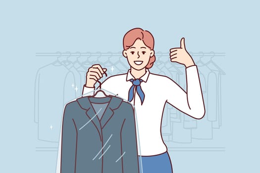 Woman employee of cleaning salon demonstrates jacket in plastic film and shows thumbs up. Girl working in cleaning salon invites people who want to clean dirty clothes with professional detergents