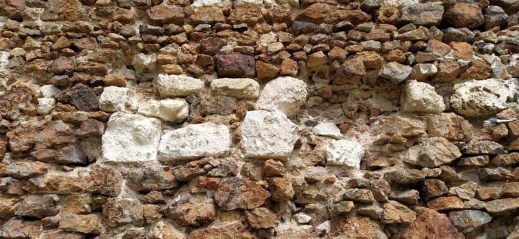 Stone wall. Stacked large bricks and cobblestones in warm colors. Loose white stones protruding from the surface of the wall. Tower in Vrdnik, Serbia