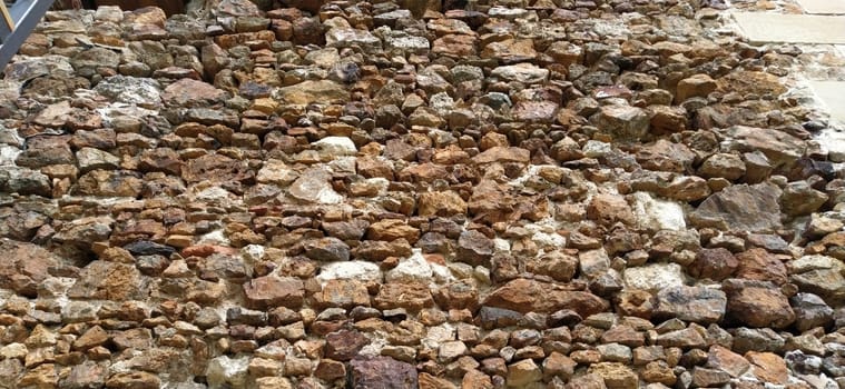 Stone wall. Stacked large bricks and cobblestones in warm colors. Loose white stones protruding from the surface of the wall