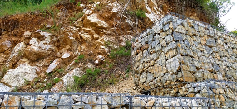engineering protection against landslide and landslide processes in road construction. Protection against collapse of soil and stones on the road. Stones placed in metal frames.