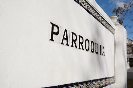 Parish sign in spanish with glazed tiles over whitewashed wall. Selective focus