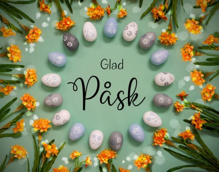Flat Lay With Swedish Text Glad Pask Means Happy Easter. Easter Egg Decoration With Orange Spring Flowers. Light Green Paper Background With Bright And Shiny Light Effect.