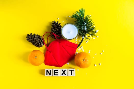 Tangerines lie in medical mask among the branches of the Christmas tree, word Next wooden cubes