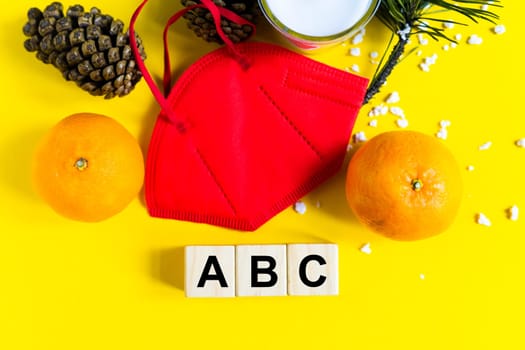 Tangerines lie in medical mask among the branches of the Christmas tree, word Abc wooden cubes