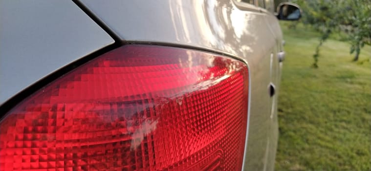 Detail of the rear end of a silver car with focus on the brake lights. Red rear light of the car. Brake signal for the driver driving behind.