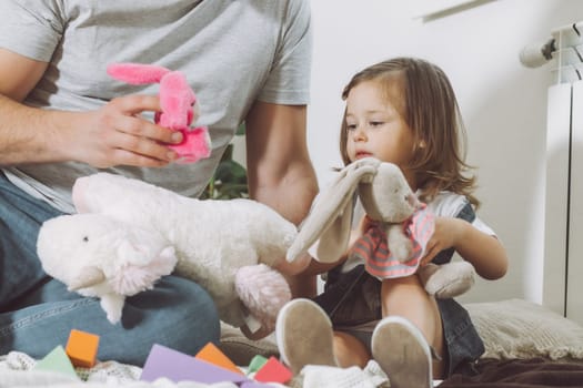 Dad and little girl 2-4 play with soft toys sitting on floor at home