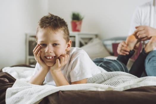 Father plays with his son 7-10 on bed. Dad tickles kids feet. Family having fun