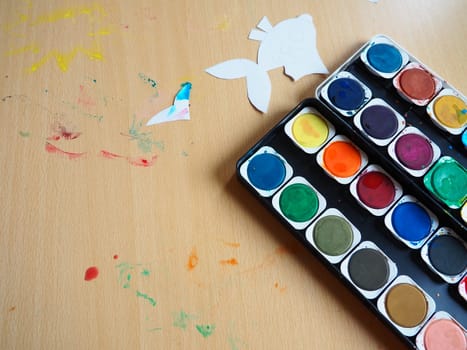 Desktop with drawing tools. A set of watercolor paints. Paper-cut, painted fish figurines. View from above. Lesson or creative task.