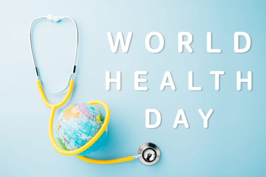 World Health Day. Top view yellow doctor stethoscope wrapped around world globe isolated on pastel blue background with copy space for text, Global healthcare, Health care and medical concept