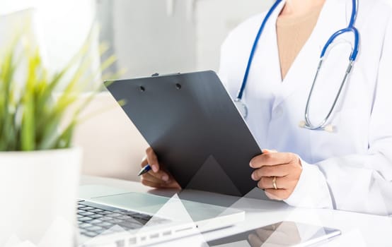 Doctor Day Concept. Nurse in uniform with doctor stethoscope writing information of patient prescription medical in paperwork checklist on clipboard on front laptop, Medical and Health care insurance