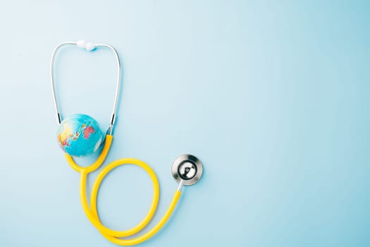World Health Day. Top view yellow doctor stethoscope wrapped around world globe isolated on pastel blue background with copy space for text, Save world day, Health care and medical concept