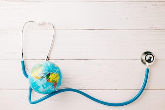 World Health Day. Top view blue doctor stethoscope wrapped around world globe isolated on white wood background with copy space for text, Global healthcare, Health care and medical concept