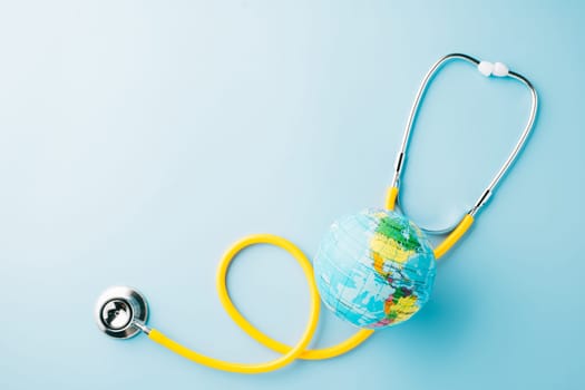 World Health Day Concept. Top view yellow doctor stethoscope and world globe isolated on pastel blue background with copy space, Save world day, Environment Green Earth, Health care and medical