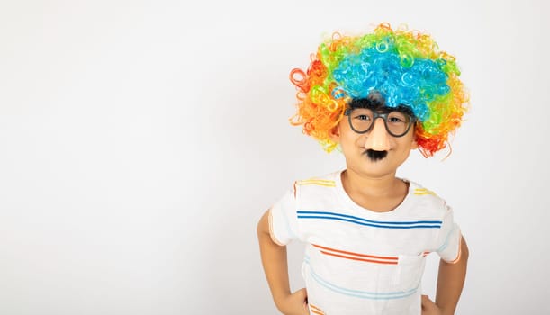 April Fool's Day. Portrait of Funny kid boy clown wears a curly wig colorful a big nos and glasses and has a mustache isolated on white background with copy space, Happy child festive decor