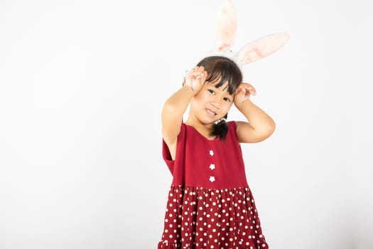 Happy Easter Day. Smile Asian little girl wearing bunny ears make hands act like a rabbit studio shotr isolated on white background with copy space, Easter eeasonal sale and discount