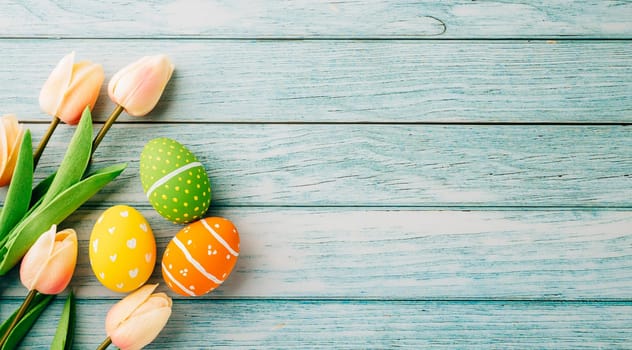 Happy Easter Day Concept. Flat lay holiday banner background web design white colorful easter eggs painted with tulips flowers on blue wood background with empty copy space, overhead, template